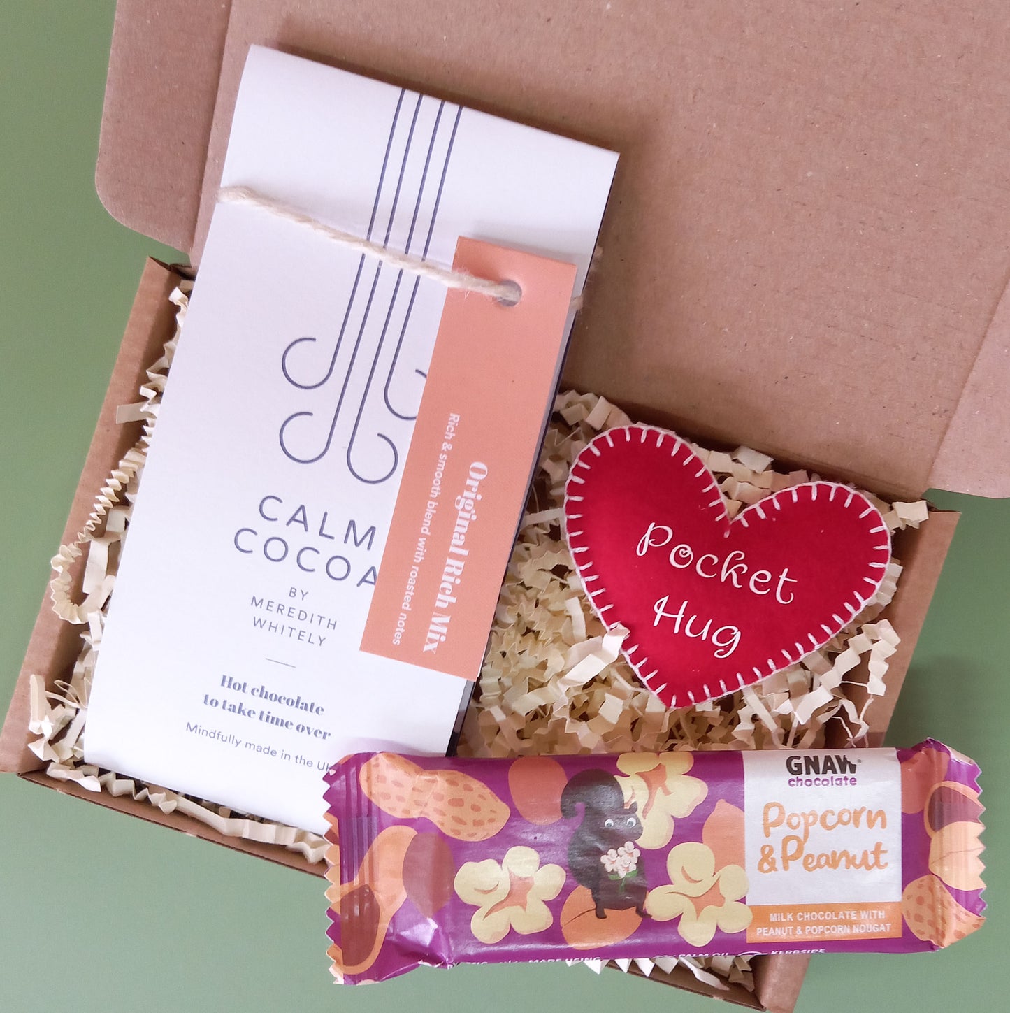 A gift box containing hot chocolate, popcorn and peanut milk chocolate and a felt heart-shaped pocket hug
