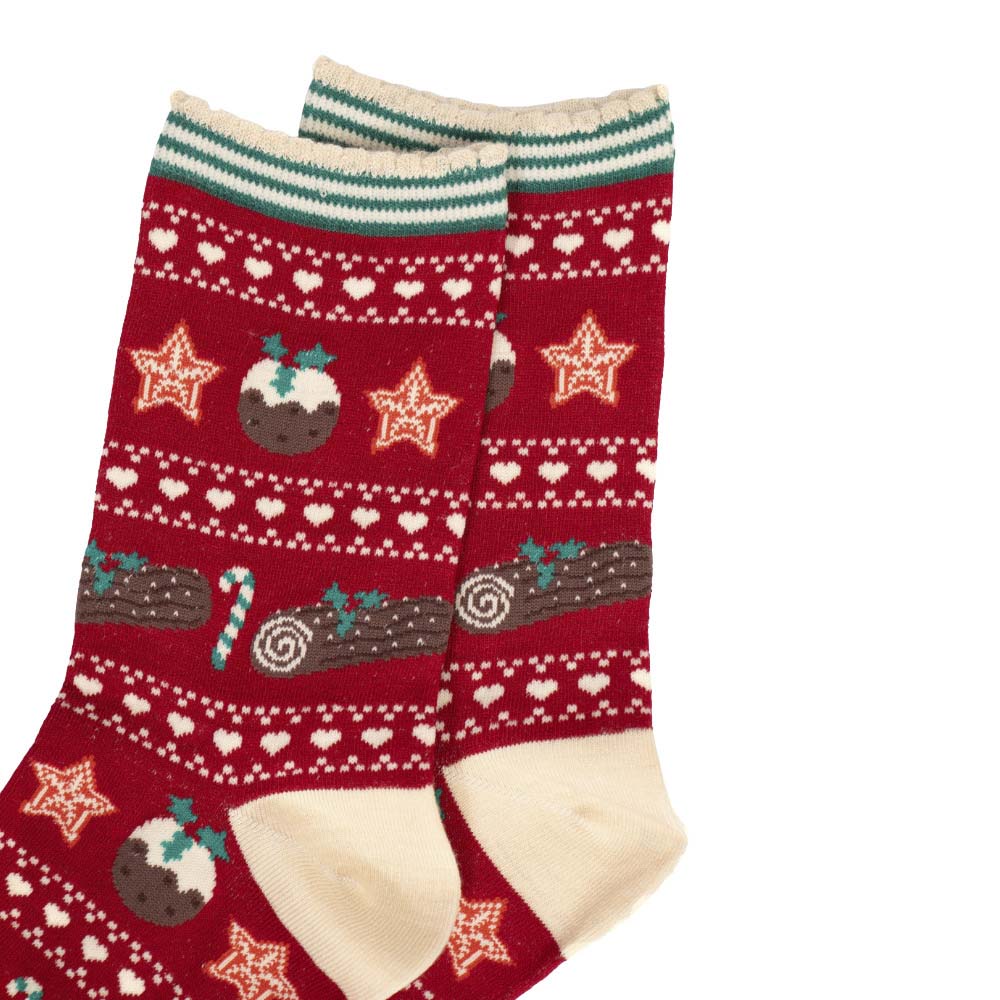 Close-up of a pair of red ladies' socks featuring cream cuffs and heels with green accents and a Christmas pudding and yule log repeating pattern