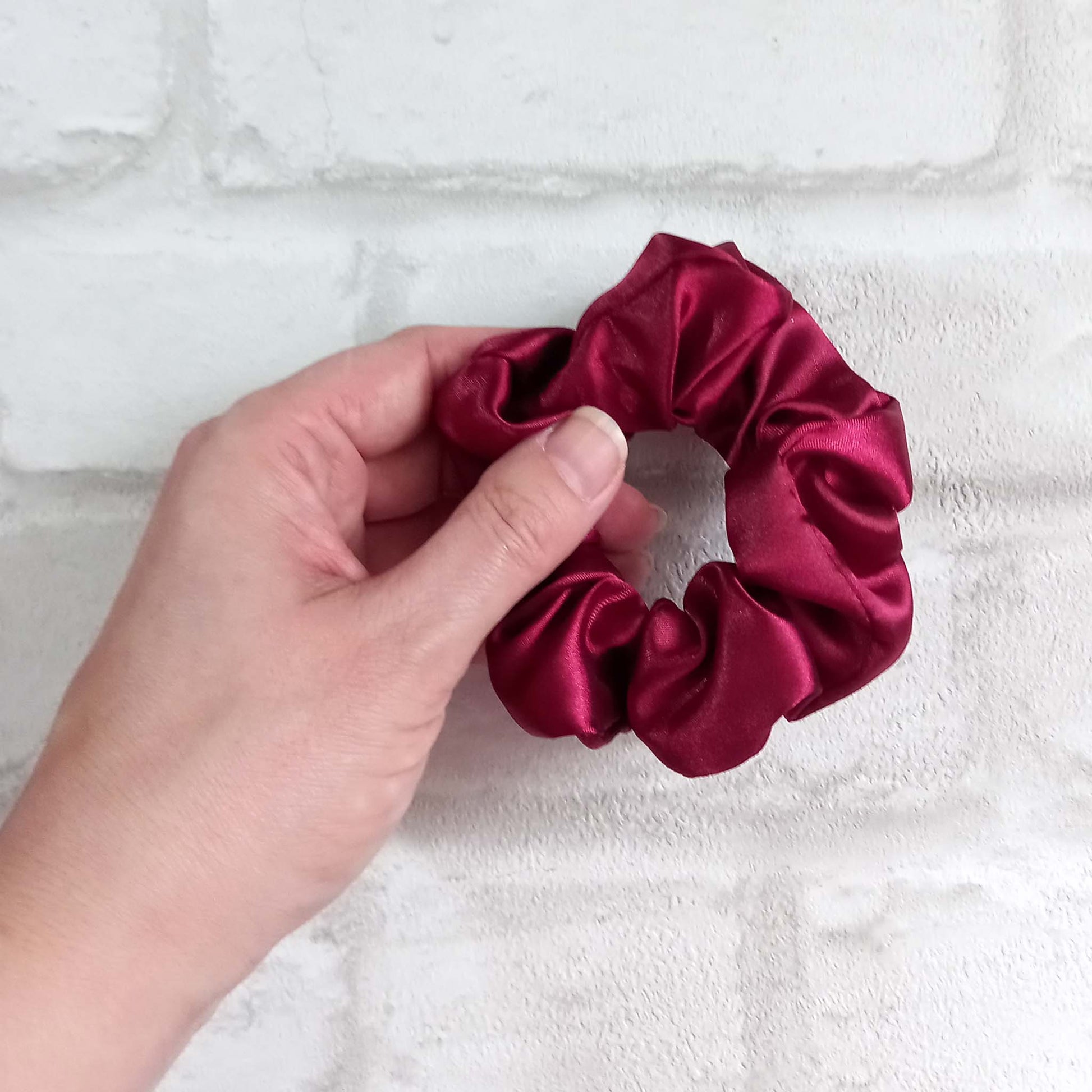 Hand holding a burgundy satin hair scrunchie