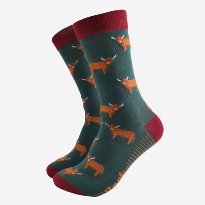 A pair of men’s green and red socks featuring highland cows