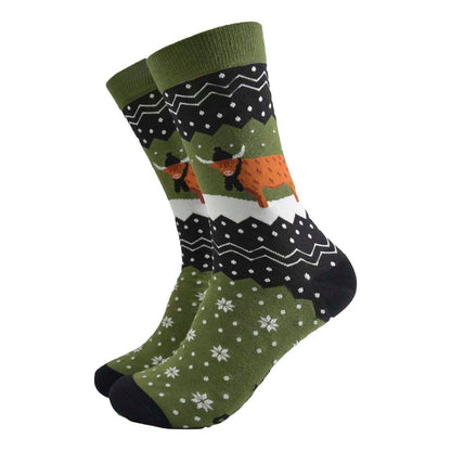 A pair of olive green and black socks featuring snowflakes and a highland cow wearing a hat and scarf