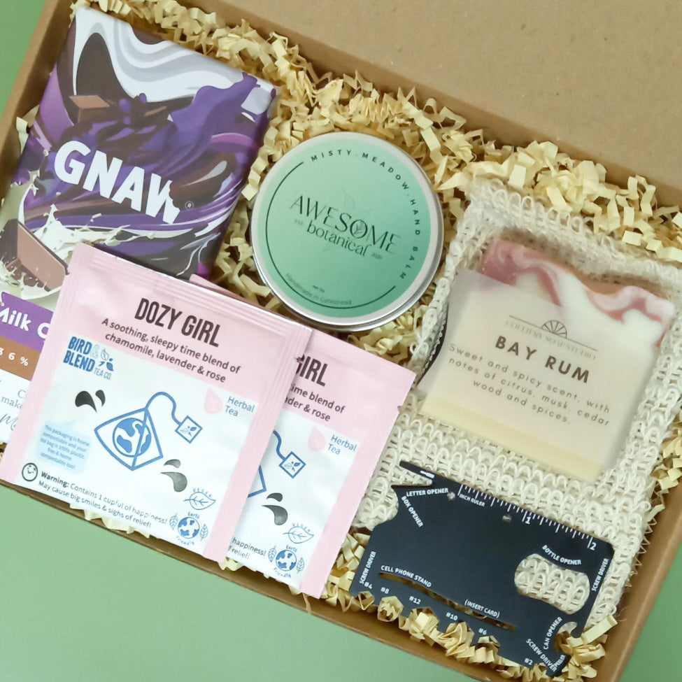 Gift box containing bar of chocolate, solid hand balm, sisal soap saver pouch, soap bar, herbal teas and credit card multi tool