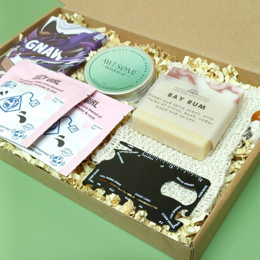 Gift box containing bar of chocolate, solid hand balm, sisal soap saver pouch, soap bar, herbal teas and credit card multi tool
