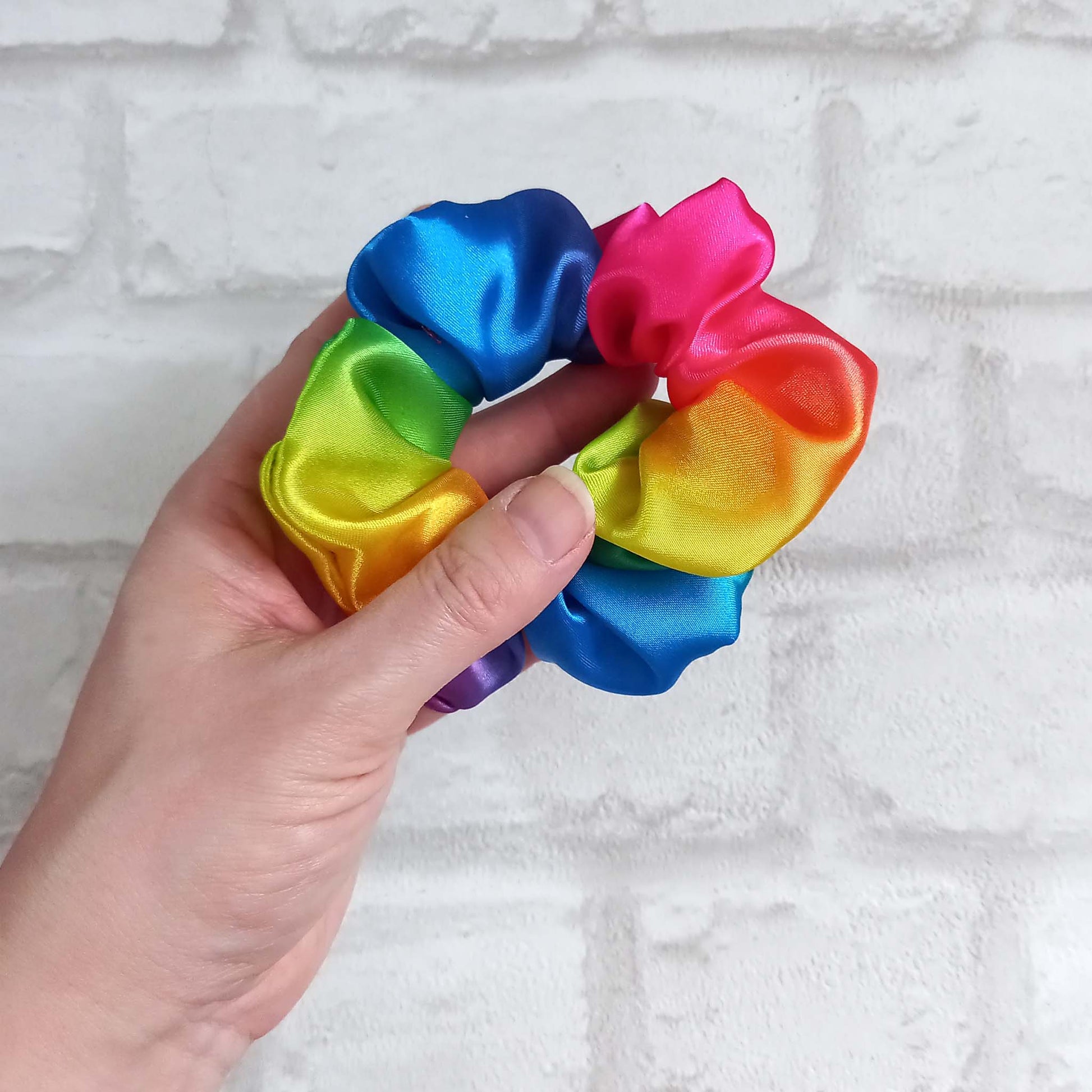 Hand holding a rainbow satin hair scrunchie