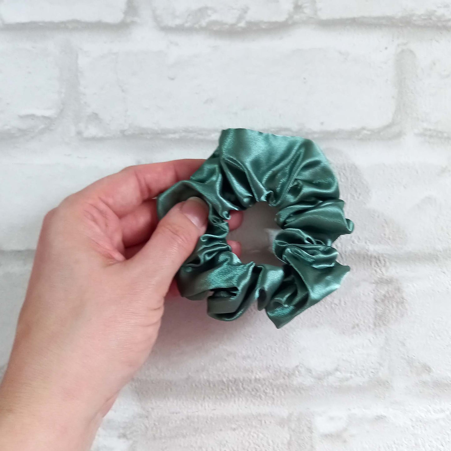 Hand holding a sage green satin hair scrunchie