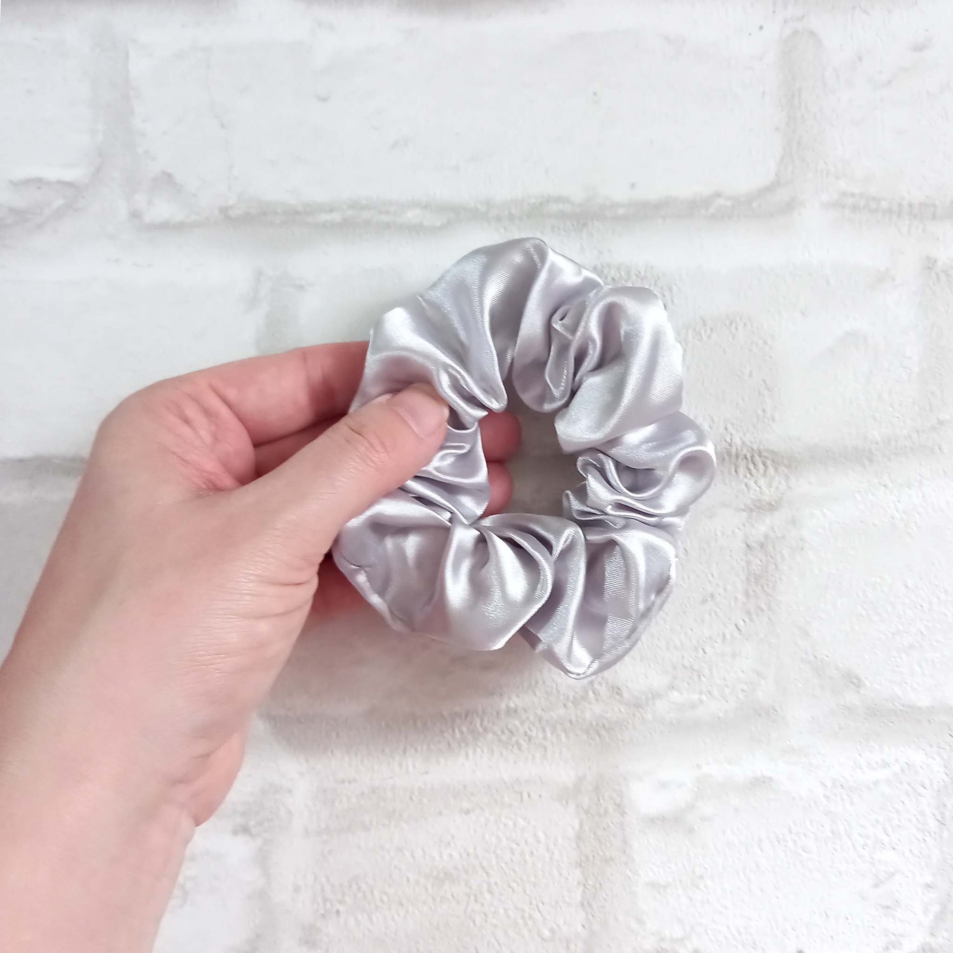 Hand holding a silver satin hair scrunchie