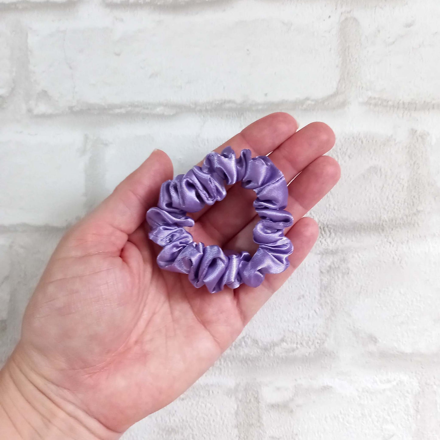 Hand holding skinny lilac satin hair scrunchie