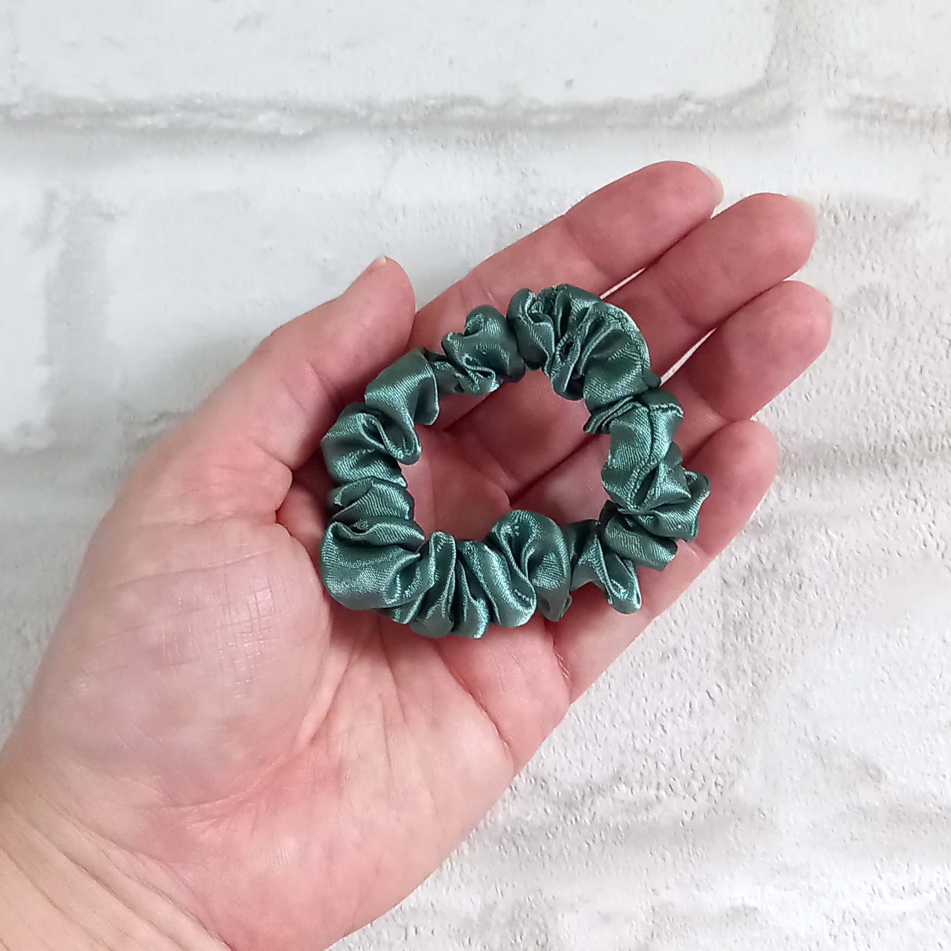 Hand holding skinny satin sage green hair scrunchie