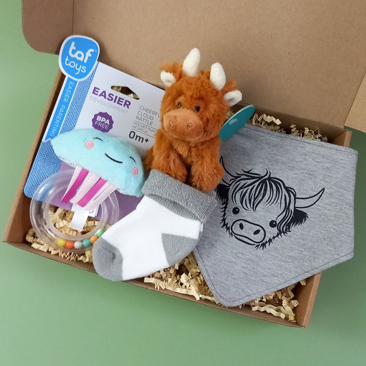 New baby gift box containing a mini soft toy highland cow, a pair of baby socks, a highland cow themed dribble bib and a cloud shaped rattle