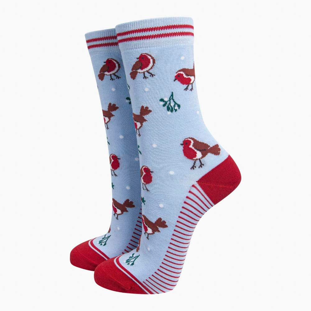 A pair of light blue socks with red heels and toes with a repeating pattern of robins, holly and mistletoe