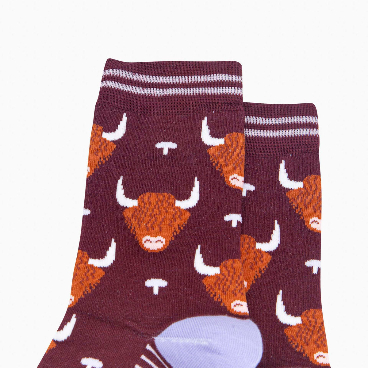 A pair of crew socks in dark burgundy with an orange and white highland cow pattern, featuring lilac stripes at the cuffs and a light lavender heel and toe cap.
