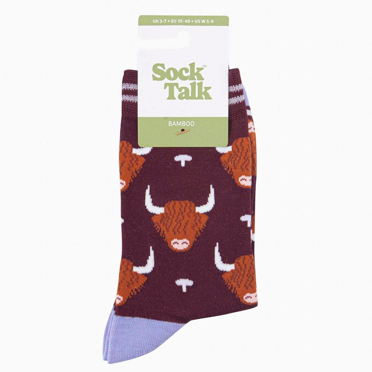 A pair of packaged Sock Talk bamboo crew socks with a highland cow print, featuring a dark burgundy base with orange and cow faces, a light purple toe, and a white paper hanger label.