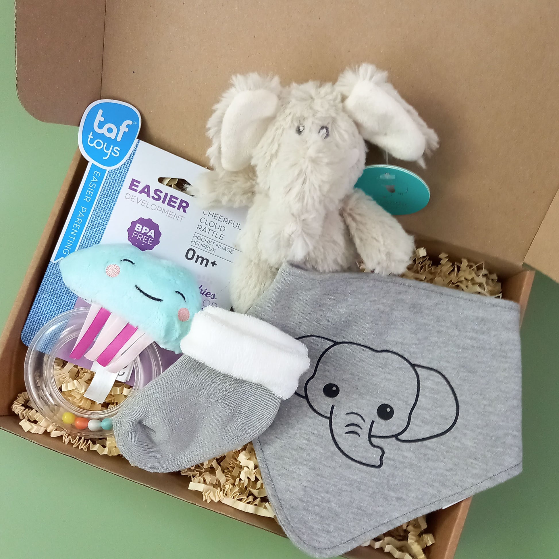 A box containing a cloud rattle, a pair of baby socks, and small soft toy elephant and an elephant design bib